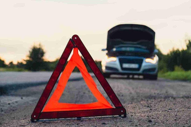 Driver waiting safely on the roadside with a warning triangle placed front a broken-down car.