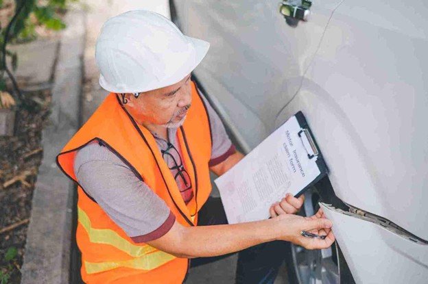 Technician in a safety vest documenting vehicle condition on a clipboard during inspection
