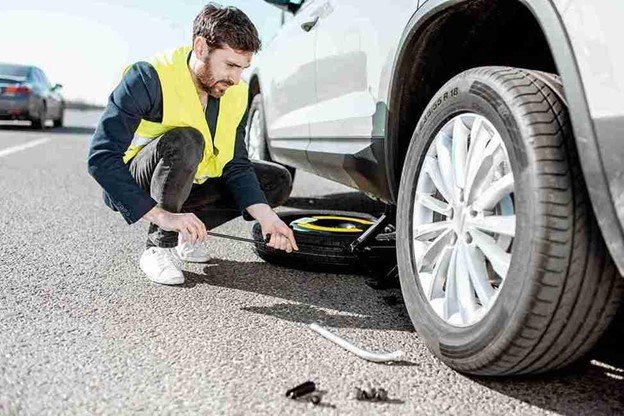 man checking a flat tire on a white car stopped along the roadside