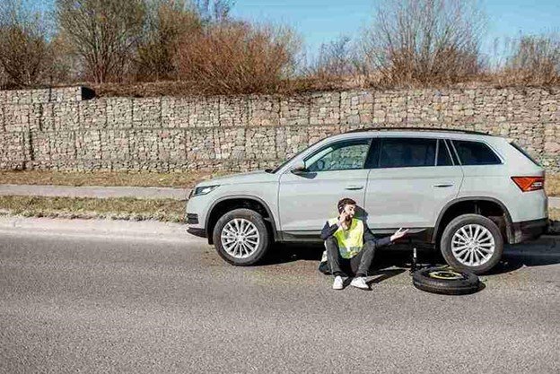Tow truck operator standing beside a vehicle secured on a flatbed after roadside recovery