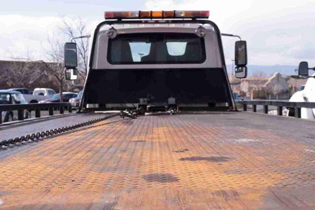 Tow truck operator standing beside a vehicle secured on a flatbed after roadside recovery