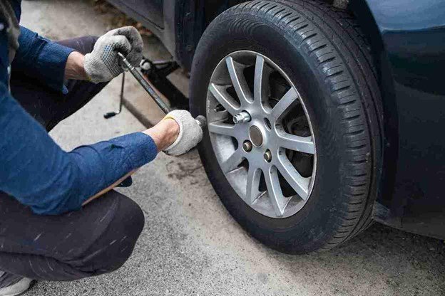 Man using a lug wrench to loosen wheel nuts during a step-by-step tire change process on the roadside