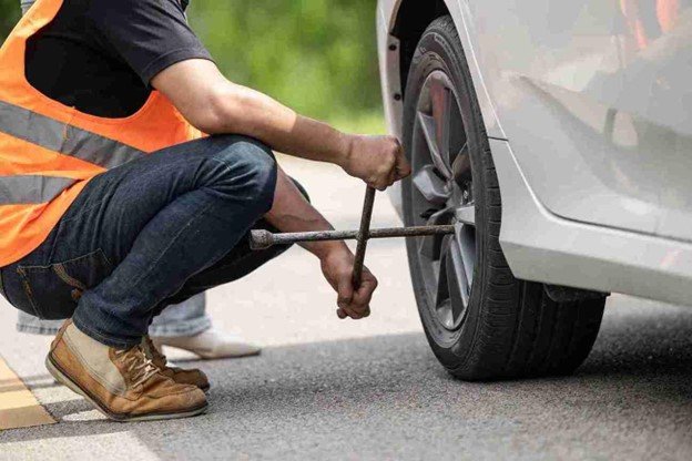 Man using a lug wrench to loosen wheel nuts during a step-by-step tire change process on the roadside