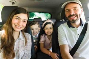 Family smiling inside their car while driving together on a sunny day
