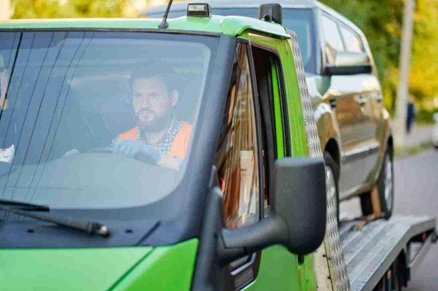 Green pickup truck loaded on a flatbed tow truck in a parking area