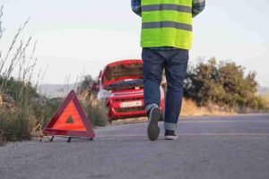Roadside worker placing a reflective warning triangle behind stopped vehicles