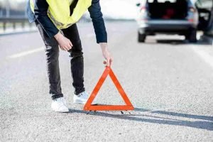 Reflective warning triangle on the road with a car stopped ahead